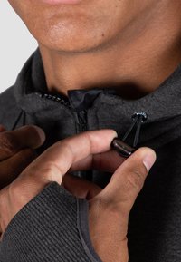Dark gray zip-up hoodie with a high collar, featuring black drawstrings and a metallic toggle. Thumbholes in the sleeves.
