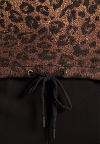 Tissu imprimé léopard marron avec cordon noir noué en un nœud papillon sur un tissu noir uni en dessous.