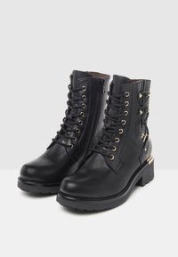 Black leather ankle boots featuring a lace-up front, gold-toned hardware, side zippers, and decorative studs on the outer side.