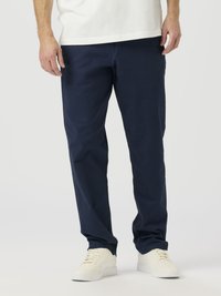 Pantalones en azul marino de corte recto hechos de tejido de algodón. Presentan un frente plano, bolsillos laterales y se combinan con zapatillas blancas.