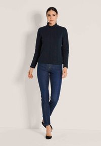 Navyfarbener Struktur-Pullover mit hohem Kragen, kombiniert mit schmalen dunklen Jeans und schwarzen Absätzen. Verfügt über ein markantes Zopfmuster.