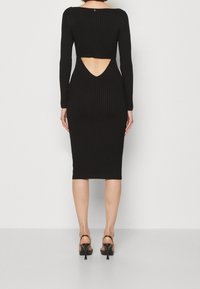 Robe noire côtelée à manches longues, avec un décolleté découpé dans le dos et une longueur midi ajustée. Présente un design épuré et une texture douce.