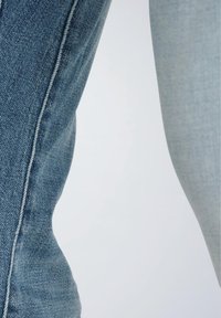 Hellblaue Jeans mit schmaler Passform. Auffällige Details sind die gesteppten Nähte und die glatte Stofftextur.