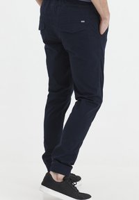 Navy blue elastic-waist pants with side and back pockets, tapered legs, and ribbed cuffs, paired with black sneakers and white soles.