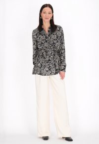 Blusa in stampa paisley bianca e nera con maniche lunghe, scollatura con bottoni e vita con cintura, abbinata a pantaloni a gamba larga crema.