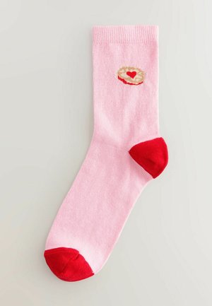 Rosafarbene Baumwollsocke mit rotem Fersen- und Zehenbereich. Mit einem cremefarbenen runden Design, das in der Mitte ein kleines rotes Herz zeigt.