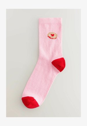 Rosafarbene Baumwollsocke mit rotem Fersen- und Zehenbereich. Mit einem cremefarbenen runden Design, das in der Mitte ein kleines rotes Herz zeigt.