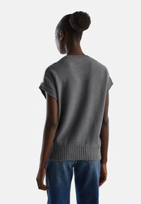 Šedý krátký pletený svetr s žebrovaným lemem, s texturovaným povrchem a volným střihem. Nošený s modrými džínami.