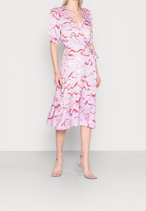 Vrouw draagt een midi wikkeljurk met roze, rode en witte wervelpatronen en lila hoge hakken met doorzichtige blokhakken.