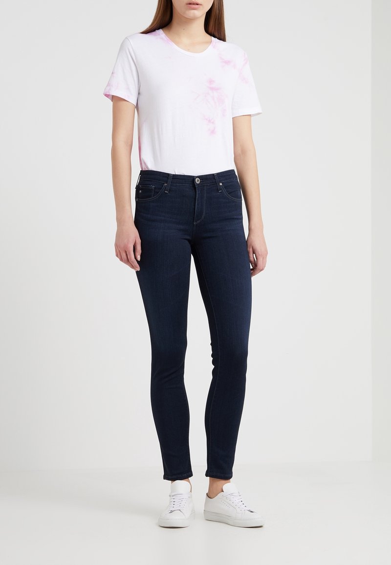 Vit t-shirt med rosa tie-dye detaljer, kombinerad med mörkblå skinny jeans. Outfiten fulländas med vita sneakers.