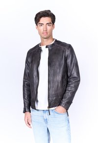 Giacca bomber in pelle nera con scollo rotondo, cerniera frontale e dettagli di cucitura sottili. Indossata sopra una camicia bianca e abbinata a jeans chiari.