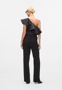 Svart jumpsuit med en volangaxel, utformad med en figurnära bodice och vida byxor. Slät tygkvalitet med en elegant look.