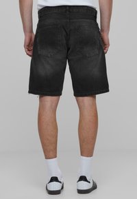 Pantalones cortos de mezclilla negra con un dobladillo deshilachado, cinco bolsillos y un ajuste clásico. La vista trasera muestra un sutil desgastado y detalles de costura.