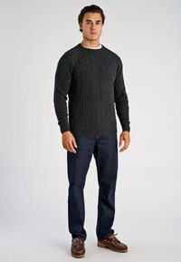 Ciemnoszary sweter w warkocze z okrągłym dekoltem i ściągaczami na rękawach, w połączeniu z ciemnoniebieskimi dżinsami i brązowymi sznurowanymi butami.