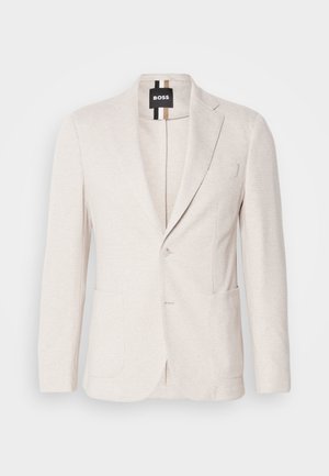 Blazer bege claro feito de tecido texturizado, com lapela recortada, dois bolsos frontais e fechamento com um único botão. Etiqueta da marca visível no interior.