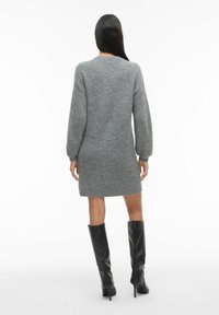 Siva pletena obleka z dolgimi rokavi, do kolen, z rebrasto teksturo. V kombinaciji z sijočimi črnimi škornji do kolen.