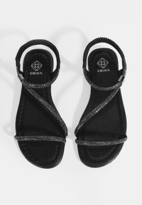Schwarze Sandalen mit einer strukturierten Stoffsohle, ausgestattet mit überkreuzten Riemen, die mit metallischen Akzenten verziert sind, und einem geflochtenen Knöchelriemen.