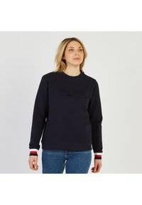 Pull navy fabriqué en tissu doux, avec un col rond, des manches longues et des poignets rayés contrastés. Texte brodé sur le devant.