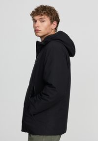 Giacca nera da esterno con cappuccio, dotata di chiusura con zip, tasche laterali e una texture liscia; design semplice senza motivi visibili.
