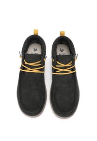 Zapatos de ante negros estilo mocasín con cordones amarillos, suelas grises y lengüetas, mostrados desde arriba sobre un fondo blanco.