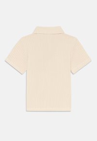 Short-sleeve polo shirt in light beige, featuring a textured knit pattern and a classic collar. The fabric is soft and breathable.