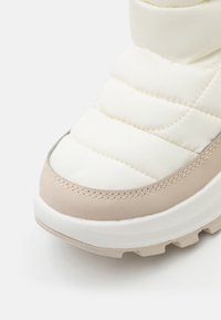 Kremfargede og beige polstrede støvler med glatt syntetisk overdel, broderte detaljer og strukturert gummisåle. Har rund tå og polstret krage.