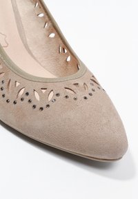 Chaussure plate en daim beige avec bout pointu, découpes décoratives et petits strass noirs le long du bord supérieur.