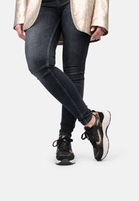 Des baskets noires et dorées avec un dessus texturé, une semelle intermédiaire blanche et des lacets. Portées avec un jean skinny noir et un blazer doré brillant.