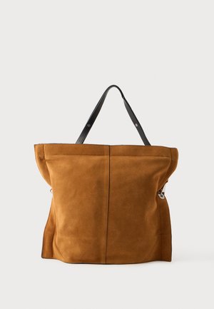 Sac cabas en daim marron doux avec des anses en cuir noir et une simple couture verticale au centre, posé sur un fond uni.