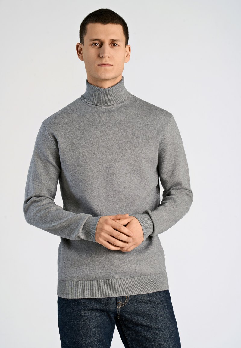 Grauer Rollkragenpullover aus weichem Strickstoff mit gerippten Bündchen und Saum, kombiniert mit dunklen Jeans. Einfaches und klassisches Design.