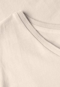 Tessuto di t-shirt color beige chiaro con una texture liscia e morbida e design a scollo a V. Il colletto presenta un bordo a costine per un tocco di dettaglio in più.