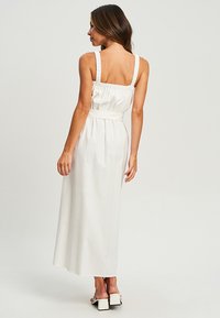 White, floor-length dress with a fitted bodice and wide elastic straps. Features a gathered back and cinched waist for added shape.