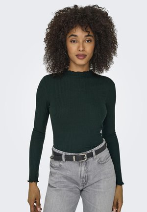 Mørkegrønn stripete langermet topp med en scalloped halslinje, kombinert med høytlagt grå jeans og et svart belte. Teksturerte stoffdetaljer synlige.