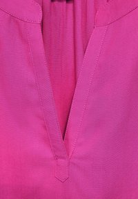 Blusa a V in tessuto fucsia vivace, con una texture liscia e dettagli di cucitura a contrasto sul colletto.