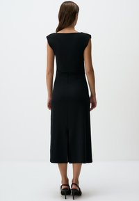 Abito midi nero con maniche a cappuccio e una leggera fessura sul retro, realizzato in un tessuto morbido. Presenta una silhouette attillata che mette in risalto linee pulite.