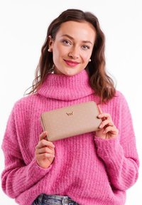 Beige wallet with embossed dots and gold logo, made of smooth material, held by a person in a pink turtleneck sweater.