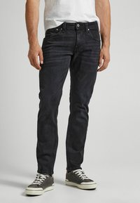 Tmavě modré džíny, slim fit s mírným vyblednutím. Přední kapsy, zipový klín a knoflíkové zapínání, spárované se šedými teniskami a bílými tkaničkami.