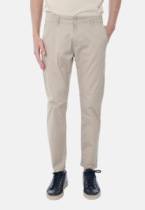 Chinos beige in cotone con una vestibilità slim, dotati di tasche laterali e chiusura con bottone; indossati con sneaker nere e una camicia dai toni neutri.