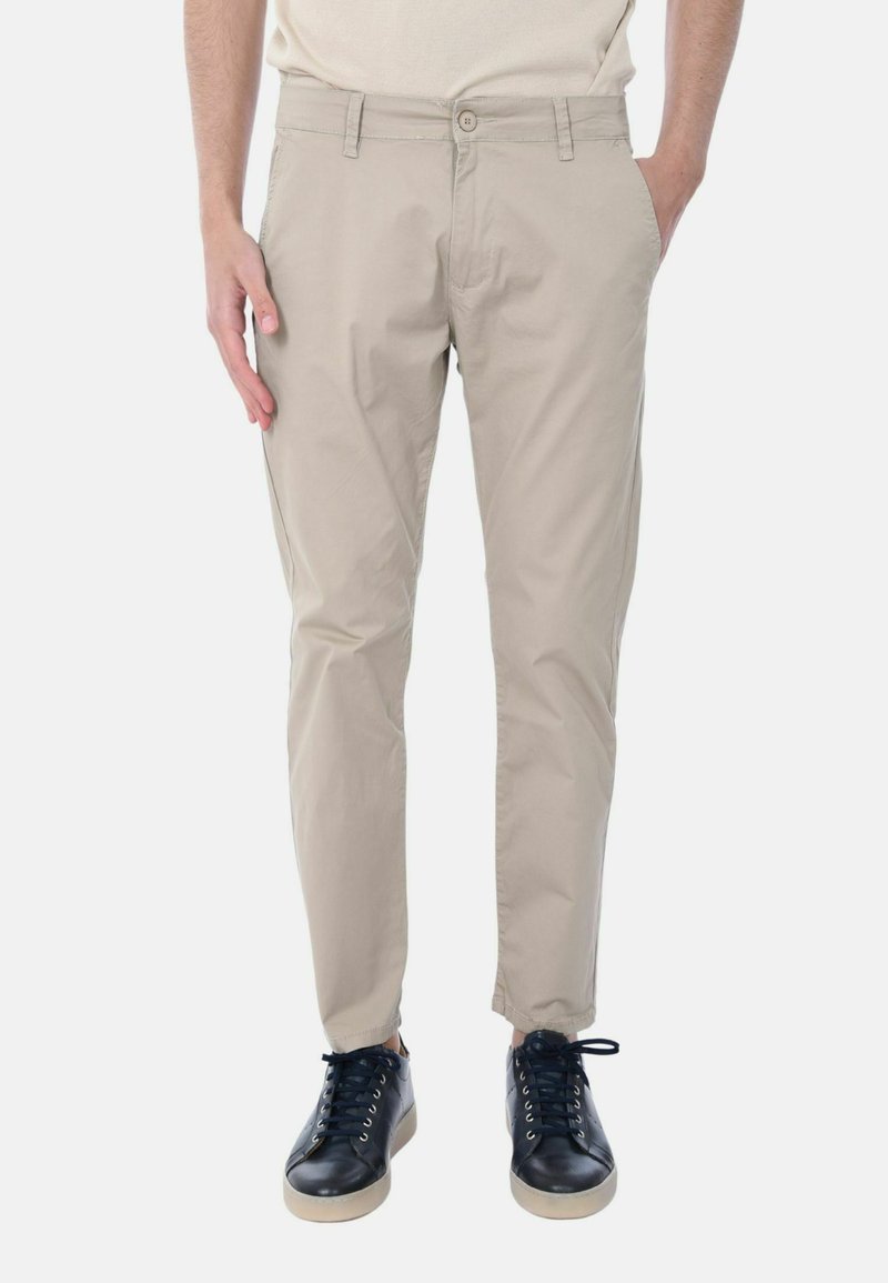 Chinos beige in cotone con una vestibilità slim, dotati di tasche laterali e chiusura con bottone; indossati con sneaker nere e una camicia dai toni neutri.