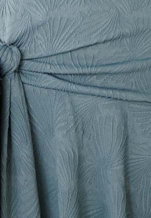 Texturovaná světle modrá látka s uzlovým detailem, s vyvýšeným vzorem připomínajícím listy nebo vlny po celé ploše.