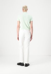 Jasnozielona koszulka polo z krótkim rękawem w połączeniu z białymi spodniami o prostym kroju i czarnymi butami. Minimalistyczny design, gładka tkanina i klasyczny krój.