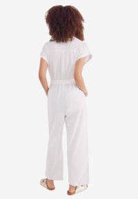 Vit jumpsuit med korta ärmar, bältad midja, vida ben, lätt material och inga synliga mönster eller detaljer.