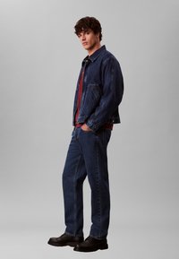 Tumesinise värvusega teksajakk ja sobivad teksapüksid, millel on lõdvestunud lõige, küljetaskud ning punane T-särk all. Komplekti lõpetavad mustad kingad.