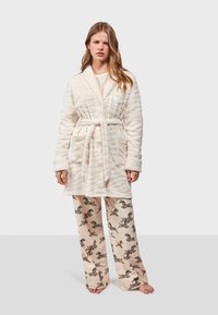 Crème gekwilt badjas met een gestructureerd ontwerp en een strikceintuur, gecombineerd met beige pyjamabroek met zwarte zebra-patronen.