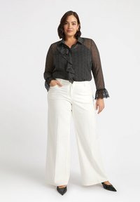 Blusa nera con pois, volant e polsini in pizzo abbinata a pantaloni bianchi a gamba larga e décolleté neri a punta.