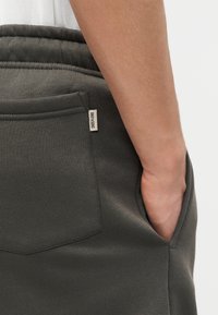Gros plan sur la main d'une personne dans la poche avant d'un pantalon de survêtement gris foncé avec une petite étiquette de marque en tissu.