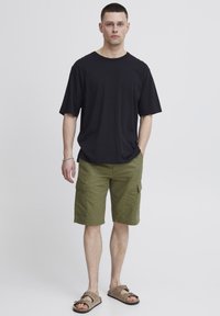 T-shirt noir à manches courtes, short cargo vert avec poches latérales et sandales brunes. Design simple, coupe décontractée, tissu léger.