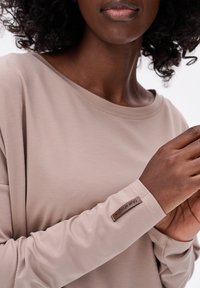 Langdurige, taupe shirt gemaakt van zacht stof, met een ronde halslijn en een label op de linker mouw. Soepele structuur en een ontspannen pasvorm.