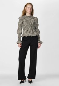 Black and white checkered blouse with puffed sleeves, textured fabric, and ruffled hem, paired with tailored black trousers and pointed heels.