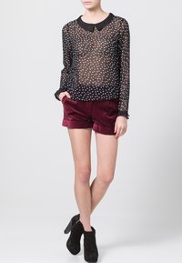 Blusa negra transparente con lunar blanco, cuello y mangas largas, combinada con pantalones cortos de terciopelo burdeos. La modelo lleva botines negros de tacón.